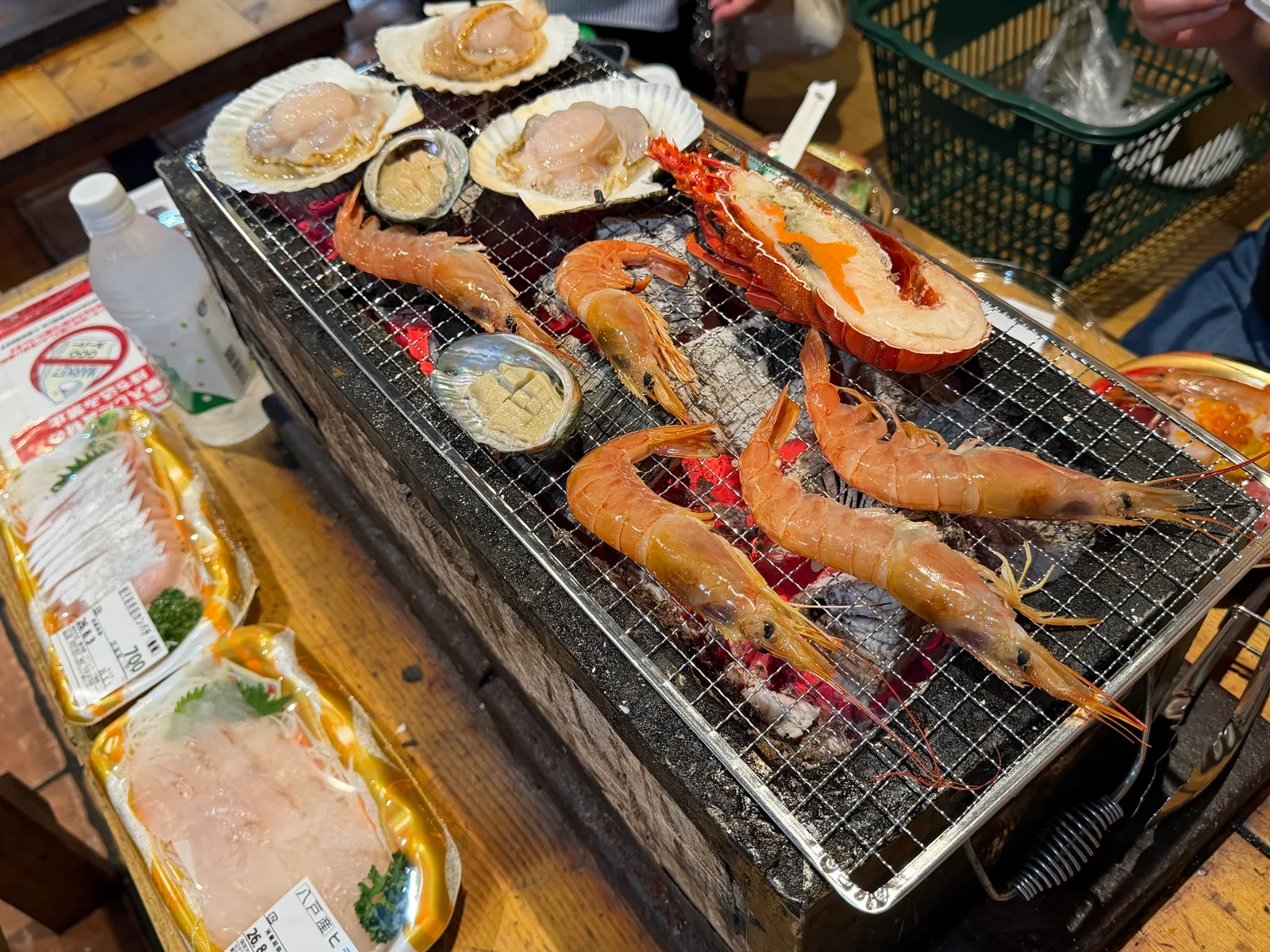 七輪の炭火で焼くホタテ・エビ・貝と、横に置いた刺身のパック
