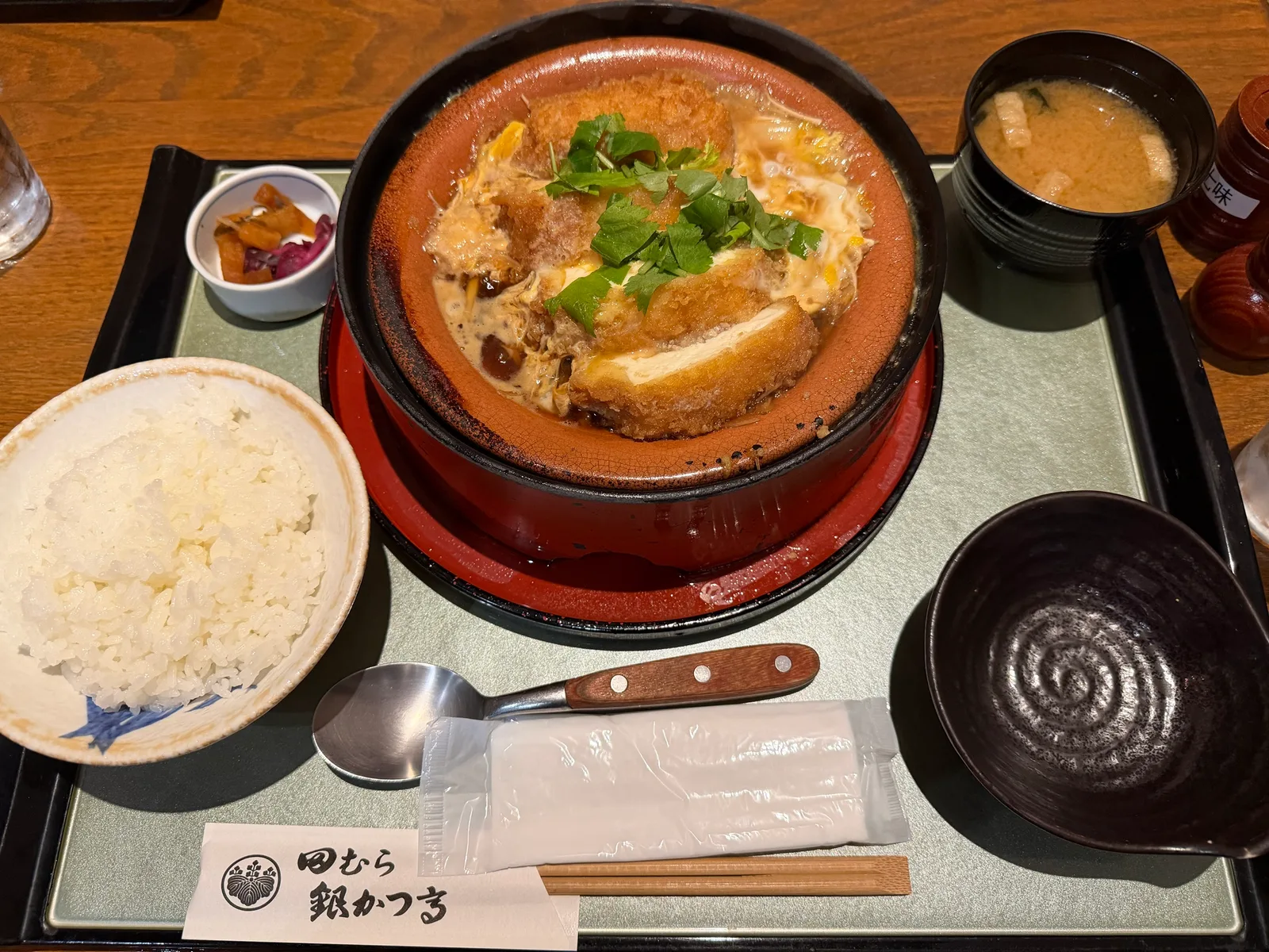 お盆にのった土鍋のかつ煮、ごはん、味噌汁、香の物